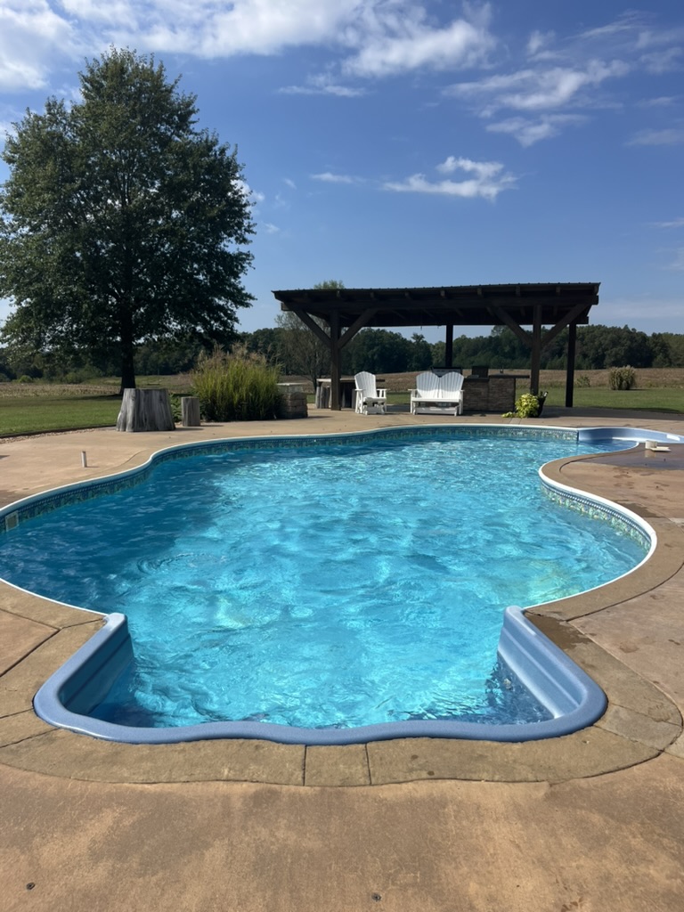 Freeform in-ground pool with a covered pergola and open Tennessee field beyond